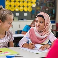 Illustration : une écolière vêtue d'un hijab à côté d'une camarade de classe. (Crédit : Ridofranz via iStock)