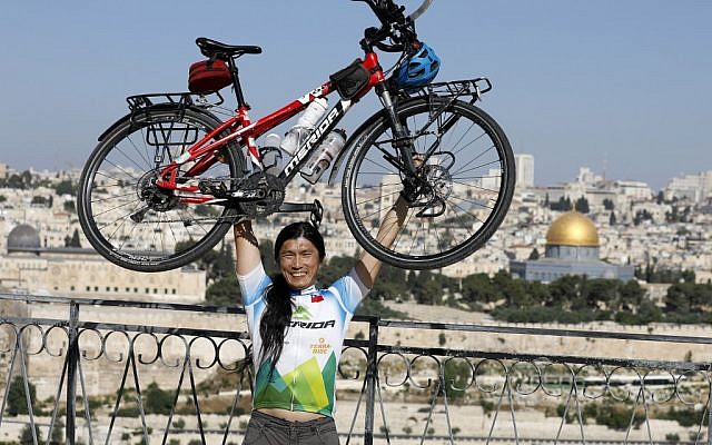 Le cycliste taïwanais qui fait le tour du monde, pose avec son vélo sur le mont des Oliviers, qui surplombe la Vieille Ville de Jérusalem, le 10 juin 2019. (Crédit : MENAHEM KAHANA / AFP)