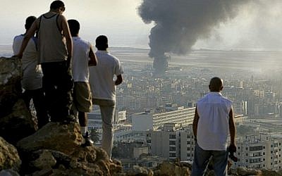 Sur cette photo datée du 14 juillet 206, des jeunes libanais sont rassemblés sur une colline surplombant la ville de Beyrouth au Liban au coucher du soleil afin d'observer la fumée qui s'échappe d'un réservoir de carburant à l'aéroport international de Beyrouth, qui a été touché par une frappe israélienne. (Crédit : Ben Curtis/AP)