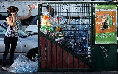Une femme jette une bouteille dans un bac de recyclage du centre de Jérusalem. (Crédit photo : Nati Shohat/Flash90)