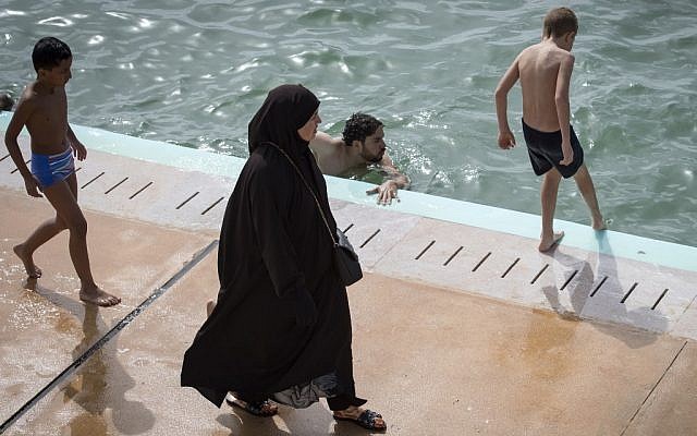 Une Marociane voile passe devant un homme à la nouvelle piscine publique de Rabat, le 7 août 2019. (Crédit ! FADEL SENNA / AFP)