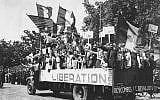 Un camion chargé de Parisiens qui brandissent des drapeaux français et américains et de panneaux "Vive De Gaulle" dans un Paris en liesse, après sa libération, le 28 août 1944. (Crédit : AP Archives)