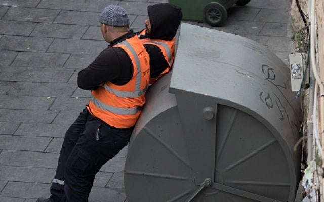 Des employés municipaux font une pause dans le centre de Jérusalem près d'une poubelle de recyclage de papier, le 26 juin 2017 (Crédit : Flash90)