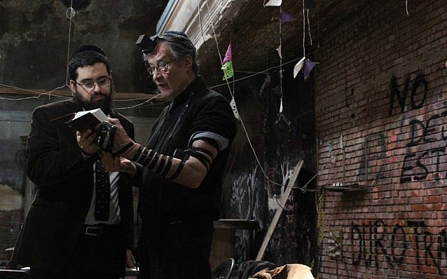 Le rabbin Shneur Mizrahi, à gauche, aide  Ricardo Aisen à prier avec des phylactères dans la synagogue du quartier de La Boca de Buenos Aires, qui vient d'être rendue à la communauté juive (Crédit : Daniel Silicaro)
