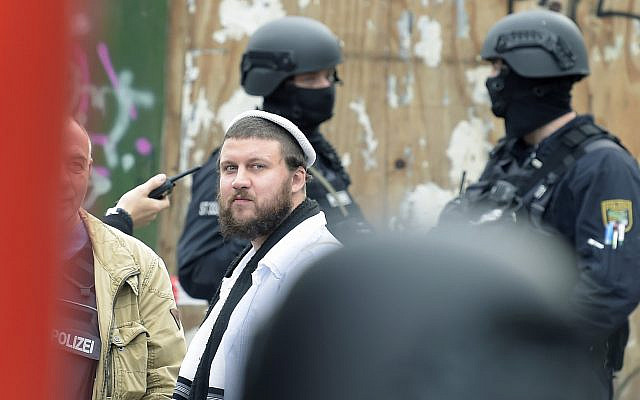 Un homme Juif entre des agents de police près du cimetière juif de Halle, à côté de la synagogue, le 9 octobre 2019. (Crédit : Jens Meyer/AP)