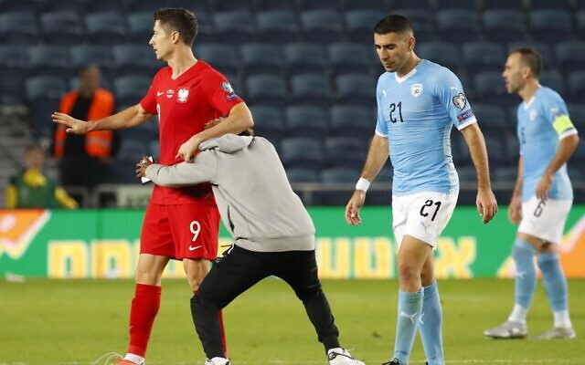 Un homme attrappe par la taille le joueur polonais Robert Lewandowski sur le terrain après une rencontre de qualification du Groupe G à l'Euro 2020 entre Israël et la Pologne au stade Teddy de Jérusalem, le 16 novembre 2019 (Crédit :  Jack GUEZ / AFP)