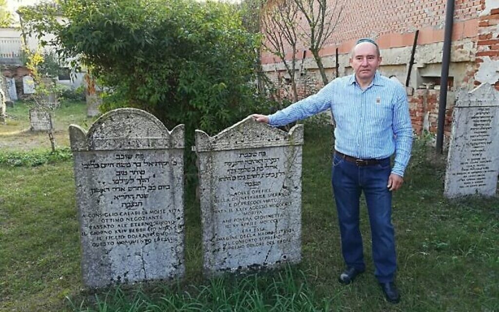 Giuseppe Minera près de deux stèles du cimetière juif d'Ostiano, en Italie (Crédit : Giovanni Vigna/ Times of Israel)