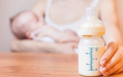 Une mère tenant son bébé dans ses bras, avec au premier plan un biberon de lait maternel. (Crédit : Pilin_Petunyia/iStock par Getty images)