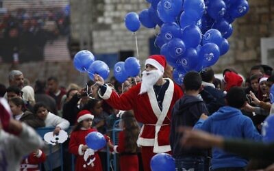 Un Palestinien déguisé en père Noël tient des ballons aux abords de l'église de la Nativité à Bethléem, en Cisjordanie, à la veille de Noël, le 24 décembre 2014 (Crédit : AP Photo/Majdi Mohammed/File)