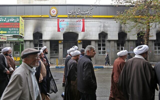 Des Iraniens passent devant une agence bancaire locale qui a été dégradée lors des manifestations contre la hausse des prix du pétrole le 20 novembre 2019 à Shahriar, à l'ouest de Téhéran. (Photo par ATTA KENARE / AFP) Des Iraniens passent devant une agence bancaire locale qui a été dégradée lors des manifestations contre la hausse des prix du pétrole le 20 novembre 2019 à Shahriar, à l'ouest de Téhéran. (Photo par ATTA KENARE / AFP)