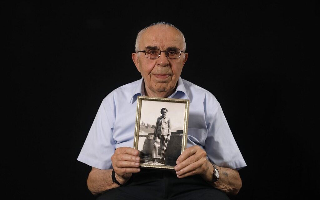 Le survivant de la Shoah Menahem Haberman, 92 ans, pose avec une photo de lui après la guerre, à son domicile de Jérusalem, le 12 décembre 2019. (Crédit : MENAHEM KAHANA / AFP)