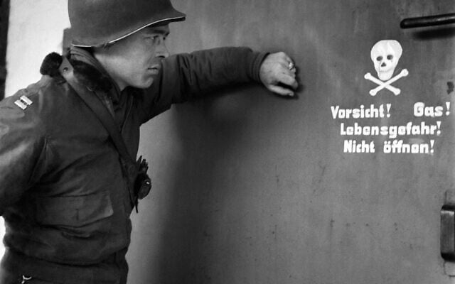 Sur cette photo prise le 29 avril 1945, un soldat américain regarde un panneau devant la porte d'une chambre à gaz du camp de concentration nazi de Dachau, lors de la libération du camp par les troupes alliées. (Crédit : ERIC SCHWAB / AFP)