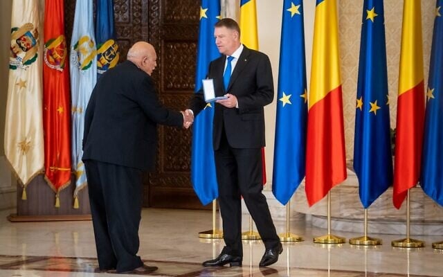 Le président roumain Klaus Iohannis rend hommage à Traian Craciun, un survivant de la Shoah rom lors d'une cérémonie marquant le 75e anniversaire de la libération d'Auschwitz-Birkenau, le 27 janvier 2020, à Bucarest, en Roumanie. (Crédit : Andrei PUNGOVSCHI / AFP)