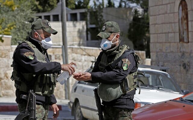 Des forces de sécurité palestiniennes portant des masques se désinfectent les mains à côté d'un hôtel qui a été bouclé dans la ville de Beit Jala suite à des cas suspects de coronavirus COVID-19, le 5 mars 2020. (Crédit : Musa Al SHAER / AFP) Des forces de sécurité palestiniennes portant des masques se désinfectent les mains à côté d'un hôtel qui a été bouclé dans la ville de Beit Jala suite à des cas suspects de coronavirus COVID-19, le 5 mars 2020. (Crédit : Musa Al SHAER / AFP)