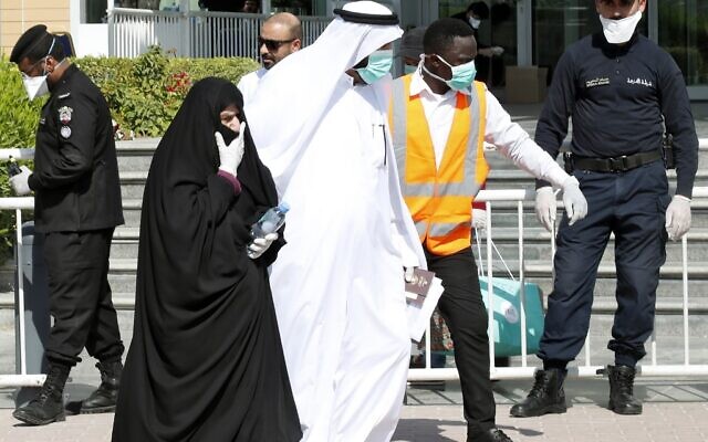 La police qatari se trouve devant un hôtel à Doha alors qu'un soignant accompagne des personnes portant des masques par crainte du coronavirus, le 12 mars 2020. (Photo par - / AFP) / Qatar OUT) La police qatari se trouve devant un hôtel à Doha alors qu'un soignant accompagne des personnes portant des masques par crainte du coronavirus, le 12 mars 2020. (Photo par - / AFP) / Qatar OUT)