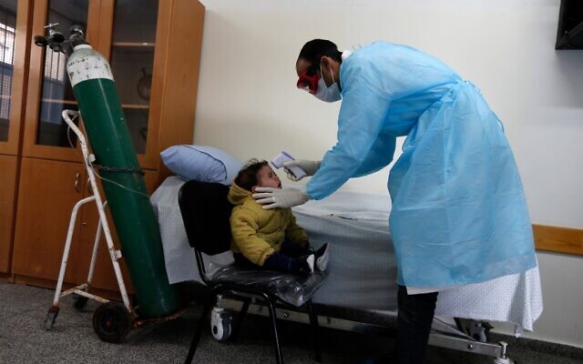 Un agent de santé palestinien portant un masque de protection vérifie la température corporelle d'un enfant dans une école de l'UNRWA dans le camp de réfugiés d'al-Shati à Gaza, le 18 mars 2020, en pleine pandémie de coronavirus. (Crédit : MAHMUD HAMS / AFP) Un agent de santé palestinien portant un masque de protection vérifie la température corporelle d'un enfant dans une école de l'UNRWA dans le camp de réfugiés d'al-Shati à Gaza, le 18 mars 2020, en pleine pandémie de coronavirus. (Crédit : MAHMUD HAMS / AFP)