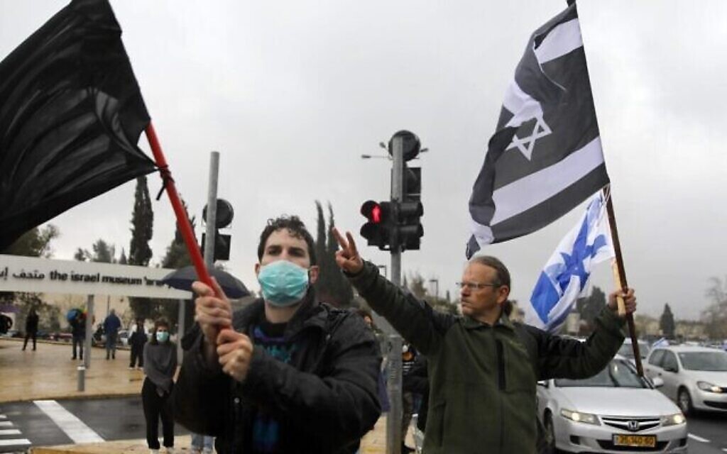 Les manifestants brandissent un drapeau noir, un drapeau israélien et un drapeau israélien aux couleurs inversées, devant la Knesset à Jérusalem, le 19 mars 2020. La manifestation s’opposait à la récente décision du président de la Knesset de fermer l’Institution pendant plusieurs jours, et contre ce qu'ils ont décrit comme des « dommages à la démocratie israélienne ». (Crédit : MENAHEM KAHANA / AFP)