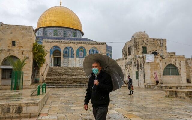 Un Palestinien portant un masque de protection contre le COVID-19, se trouve devant la mosquée du Dôme du Rocher dans l'enceinte presque déserte de la mosquée Al-Aqsa, dans la vieille ville de Jérusalem, le 20 mars 2020. (Crédit : AHMAD GHARABLI / AFP) Un Palestinien portant un masque de protection contre le COVID-19, se trouve devant la mosquée du Dôme du Rocher dans l'enceinte presque déserte de la mosquée Al-Aqsa, dans la vieille ville de Jérusalem, le 20 mars 2020. (Crédit : AHMAD GHARABLI / AFP)