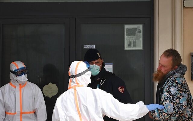 Des membres du personnel médical vêtus d'un uniforme de protection sauvent un sans-abri à Ostie, dans la banlieue de Rome, le 21 mars 2020(Crédit : Alberto PIZZOLI / AFP)