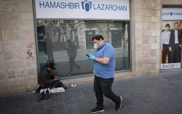 Un homme portant un masque pour se protéger du coronavirus, devant un sans-abri, près d'un centre commercial fermé à Jérusalem, le 23 mars 2020. (Crédit : Olivier Fitoussi / Flash90) Un homme portant un masque pour se protéger du coronavirus, devant un sans-abri, près d'un centre commercial fermé à Jérusalem, le 23 mars 2020. (Crédit : Olivier Fitoussi / Flash90)