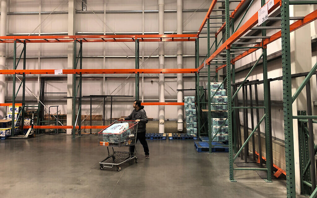Un client passe devant des rayons principalement vides et normalement remplis de papier toilette et de serviettes en papier dans un magasin Costco à Teterboro, dans le New Jersey. (Crédit : AP Photo/Seth Wenig)
