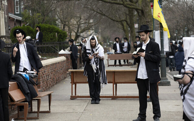 Des Juifs orthodoxes appliquent la directive de "distanciation sociale" lors d'une prière aux abords du siège mondial du mouvement Habad Loubavitch à Brooklyn, à New York, le 20 mars 2020. (Crédit : AP Photo/Mark Lennihan)