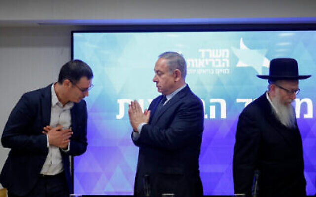 Le Premier ministre Benjamin Netanyahu, au centre, fait un geste de « namaste » envers le directeur général du ministère de la Santé Moshe Bar Siman Tov lors d'une conférence de presse avec le ministre de la Santé Yaakov Litzman (à droite) au sujet du nouveau coronavirus, au ministère de la Santé à Jérusalem, le 4 mars 2020. (Crédit : Olivier Fitoussi / Flash90) Le Premier ministre Benjamin Netanyahu, au centre, fait un geste de « namaste » envers le directeur général du ministère de la Santé Moshe Bar Siman Tov lors d'une conférence de presse avec le ministre de la Santé Yaakov Litzman (à droite) au sujet du nouveau coronavirus, au ministère de la Santé à Jérusalem, le 4 mars 2020. (Crédit : Olivier Fitoussi / Flash90)