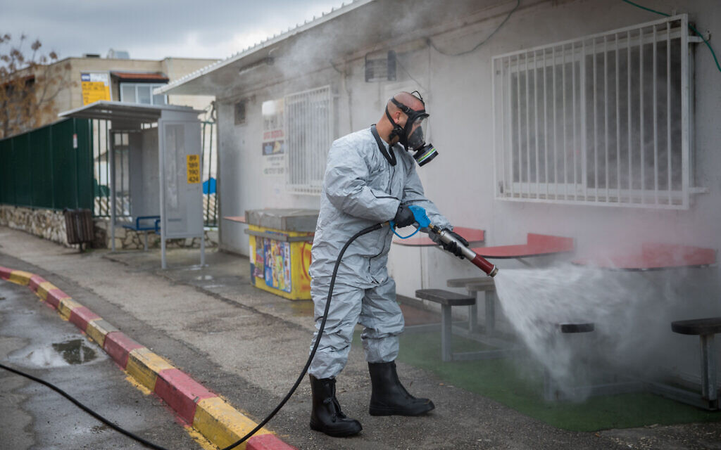 Un pompier israélien portant des vêtements de protection désinfecte une station de bus dans la ville ultra-orthodoxe de Kyriat Ye'arim (Telz-Stone), le 18 mars 2020, après que dix-sept des habitants de la ville ont contracté un coronavirus. (Crédit : Yonatan Sindel/Flash90) Un pompier israélien portant des vêtements de protection désinfecte une station de bus dans la ville ultra-orthodoxe de Kyriat Ye'arim (Telz-Stone), le 18 mars 2020, après que dix-sept des habitants de la ville ont contracté un coronavirus. (Crédit : Yonatan Sindel/Flash90)