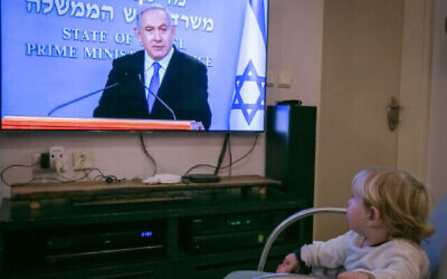 Un enfant regarde le Premier ministre Benjamin Netanyahu pendant une conférence de presse en direct sur les nouvelles restrictions gouvernementales pour la population concernant le coronavirus, le 19 mars 2020. (Chen Leopold/Flash90)