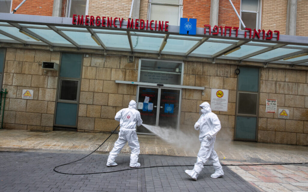 Un pompier israélien portant une tenue de protection désinfecte l'entrée des urgences de l'hôpital Hadassah Ein Karem à Jérusalem, le 22 mars 2020. (Crédit : Olivier Fitoussi/Flash90)