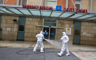 Un pompier israélien portant une tenue de protection désinfecte l'entrée des urgences de l'hôpital Hadassah Ein Karem à Jérusalem, le 22 mars 2020. (Crédit : Olivier Fitoussi/Flash90)