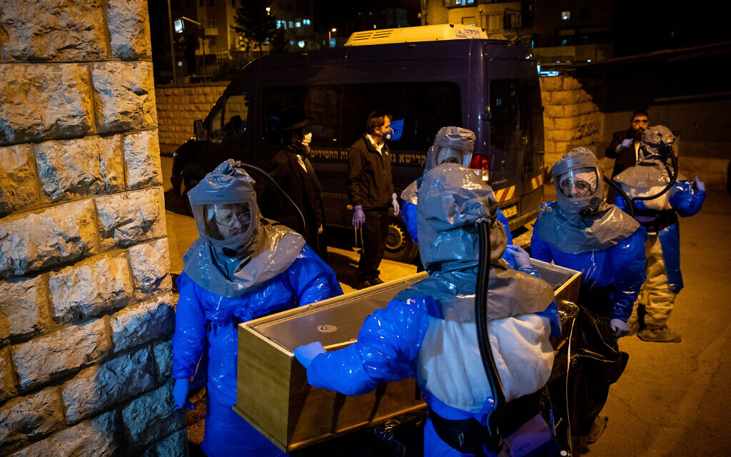 Chevra Kadisha workers wearing protective clothes, carry the body of a man died from complications of Coronavirus (COVID-19) infection, at the Shamgar Funeral Home in Jerusalem on March 24, 2020. Photo by Yonatan Sindel/Flash90 *** Local Caption *** קורונה
וירוס
חברה
קדישא
ירושלים
לבושים
בגדים
מגן
נגד