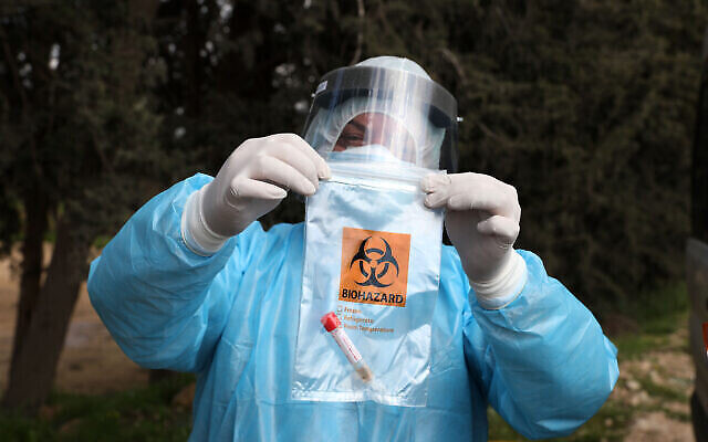 Des agents de santé palestiniens manipulent un échantillon de test de coronavirus de travailleurs palestiniens à leur retour d'Israël à un point de contrôle près d'Hébron, le 25 mars 2020. (Crédit : Wisam Hashlamoun/Flash90)