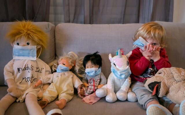 Des enfants, confinés à cause du coronavirus, jouent à mettre des masques sur leurs animaux en peluche, le 29 mars 2020. (Crédit : Chen Leopold/Flash90)
