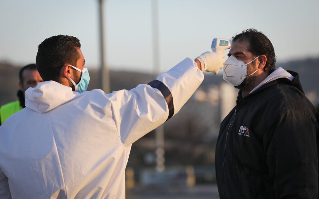 Des employés médicaux palestiniens testent les travailleurs palestiniens qui sont revenus de leur travail en Israël à l'entrée du village de Hussan en Cisjordanie, le 29 mars 2020. (Crédit : Nati Shohat/Flash90)