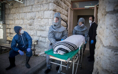 Des employés de la Chevra Kadisha portant des vêtements de protection, portent le corps d'un homme décédé des suites de complications d'une infection au Coronavirus (COVID-19), au salon funéraire Shamgar à Jérusalem, le 29 mars 2020. (Crédit : Yonatan Sindel/Flash90)
