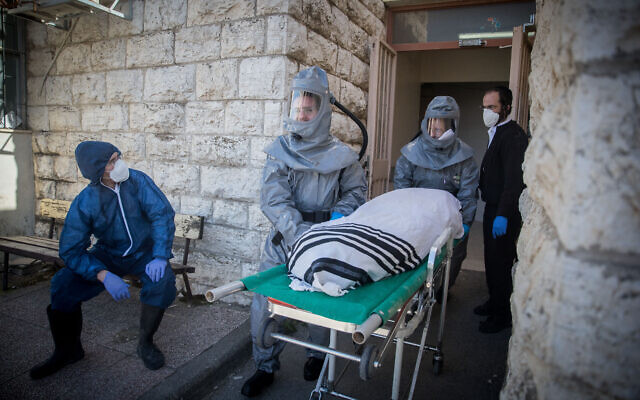 Des employés de la Chevra Kadisha portant des vêtements de protection, portent le corps d'un homme décédé des suites de complications d'une infection au Coronavirus (COVID-19), au salon funéraire Shamgar à Jérusalem, le 29 mars 2020. (Crédit : Yonatan Sindel/Flash90)