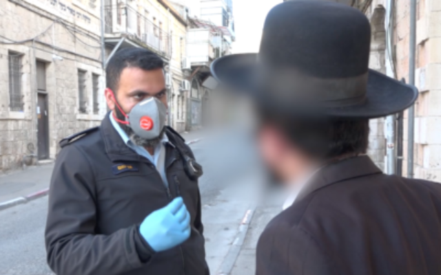 Un policier israélien donne une amende pour violation des restrictions anti-coronavirus gouvernementales dans le quartier Mea Sharim de Jérusalem, le 30 mars 2020 (Crédit : Police israélienne) Un policier israélien donne une amende pour violation des restrictions anti-coronavirus gouvernementales dans le quartier Mea Sharim de Jérusalem, le 30 mars 2020 (Crédit : Police israélienne)