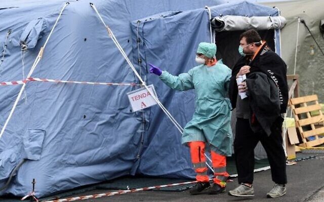 Un employé hospitalier portant un masque et un équipement de protection, accompagne un patient à l'unité de radiologie dans une structure temporaire d'urgence installée devant le service des urgences, où n'importe quel patient qui arrive en présentant les symptômes du coronavirus est testé, à l'hôpital de Brescia en Lombardie, le 13 mars 2020.
(Miguel Medina/AFP) Un employé hospitalier portant un masque et un équipement de protection, accompagne un patient à l'unité de radiologie dans une structure temporaire d'urgence installée devant le service des urgences, où n'importe quel patient qui arrive en présentant les symptômes du coronavirus est testé, à l'hôpital de Brescia en Lombardie, le 13 mars 2020.
(Miguel Medina/AFP)