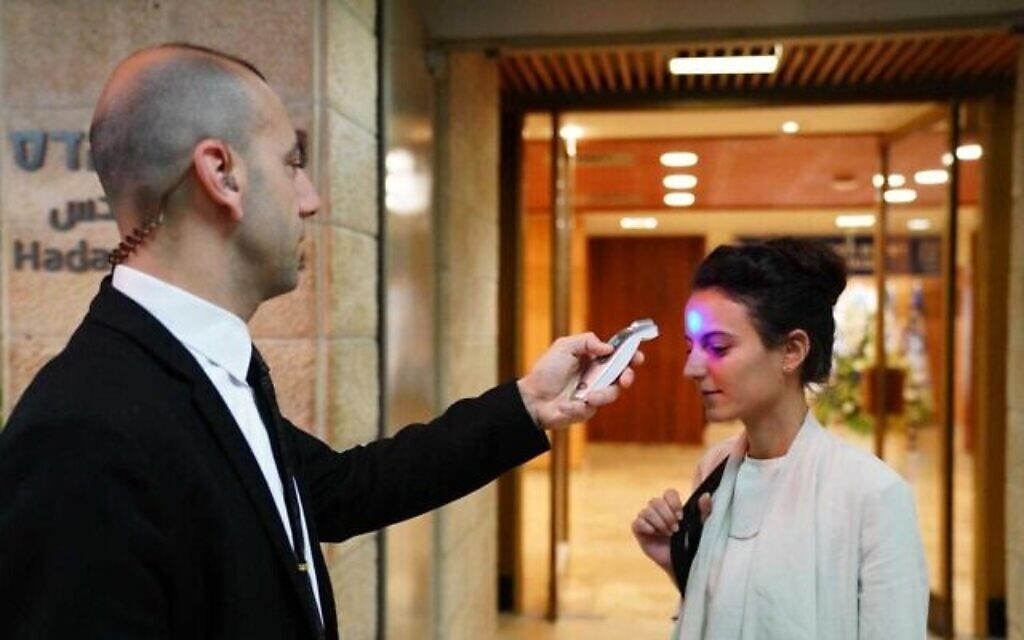 Un employé de la Knesset contrôle la température d'une femme entrant au parlement, le 16 mars 2020. (Knesset / Adina Velman) Un employé de la Knesset contrôle la température d'une femme entrant au parlement, le 16 mars 2020. (Knesset / Adina Velman)