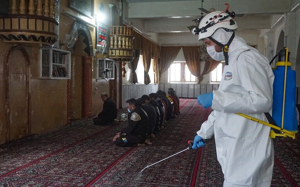 Des membres de la Défense civile syrienne, surnommés Casques blancs, font la prière du vendredi alors qu'un autre désinfecte la mosquée déserte dans la ville tenue par les rebelles de Binnish dans la province d'Idlib au nord-ouest de la Syrie, le 3 avril 2020 pendant l'épidémie de COVID-19. (Photo par Muhammad HAJ KADOUR / AFP)