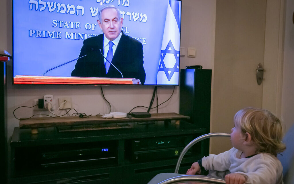 Un enfant israélien regarde le Premier ministre israélien Benjamin Netanyahu lors d’une conférence de presse en direct sur les nouvelles restrictions gouvernementales dans le cadre de la lutte contre la pandémie de coronavirus, le 19 mars 2020. (Crédit : Chen Leopold / Flash90)