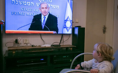Un enfant israélien regarde le Premier ministre israélien Benjamin Netanyahu lors d’une conférence de presse en direct sur les nouvelles restrictions gouvernementales dans le cadre de la lutte contre la pandémie de coronavirus, le 19 mars 2020. (Crédit : Chen Leopold / Flash90)