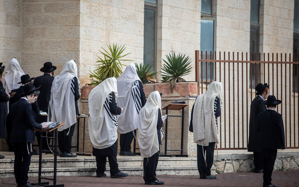 Des Juifs prient aux abords d'une synagogue dans la ville de Beitar Illit, en Cisjordanie, le 29 mars 2020 (Crédit : Aharon Krohn/Flash90)