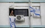 Une femme israélienne observe la rue depuis la fenêtre de sa maison dans un bâtiment décoré par des drapeaux nationaux dans la ville du sud d'Ashkelon, le 27 avril 2020. (MENAHEM KAHANA / AFP)