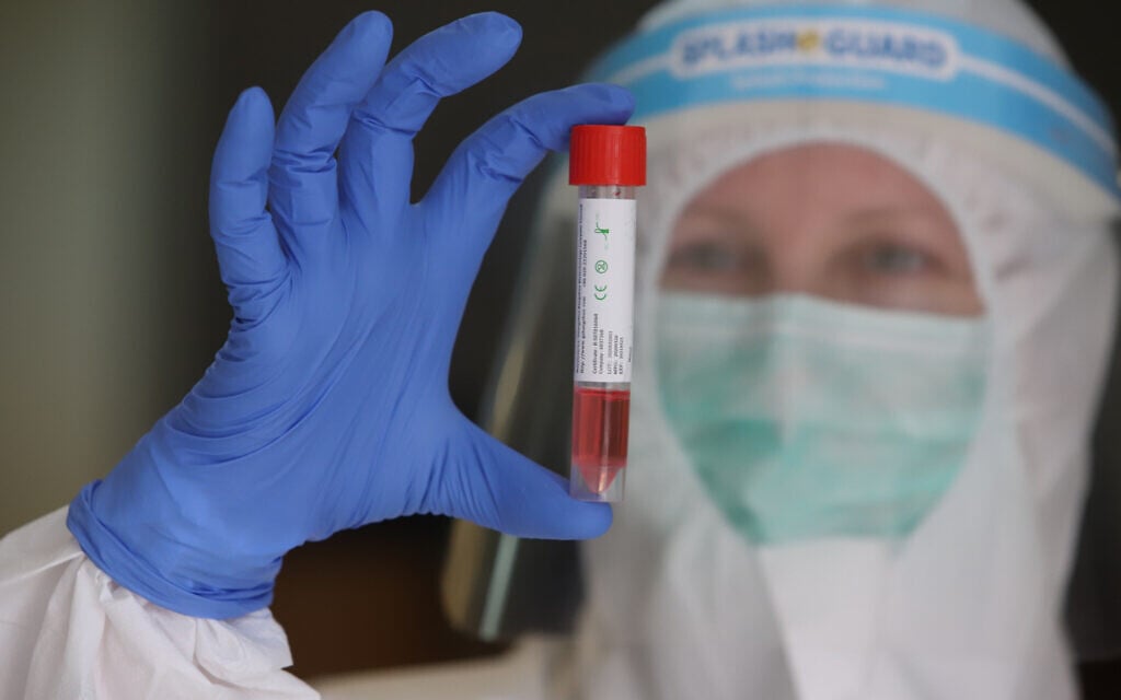 Un membre de l'équipe médicale Clalit, portant une tenue de protection, manipule des échantillons de test du COVID-19 à Lod, le 12 avril 2020. 
(Crédit : Yossi Aloni/Flash90)