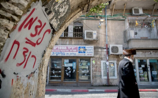 Un homme ultra-orthodoxe passe à côté d'un graffiti contre le ministre de la Santé Yaakov Litzman dans le quartier de Mea Shearim à Jérusalem le 12 avril 2020. On peut lire sur le graffiti "Litzman = meurtrier". (Yonatan Sindel/Flash90) Un homme ultra-orthodoxe passe à côté d'un graffiti contre le ministre de la Santé Yaakov Litzman dans le quartier de Mea Shearim à Jérusalem le 12 avril 2020. On peut lire sur le graffiti "Litzman = meurtrier". (Yonatan Sindel/Flash90)