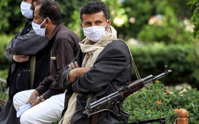 Un combattant appartenant aux rebelles houthis du Yémen porte un masque facial et des gants en latex et en lançant un fusil d'assaut à kalachnikov. Ces volontaires font partie d'une initiative communautaire visant à prévenir la propagation du COVID-19 qui se propage dans la capitale du Yémen, Sanaa, le 14 mai 2020. (Crédit : MOHAMMED HUWAIS / AFP) Un combattant appartenant aux rebelles houthis du Yémen porte un masque facial et des gants en latex et en lançant un fusil d'assaut à kalachnikov. Ces volontaires font partie d'une initiative communautaire visant à prévenir la propagation du COVID-19 qui se propage dans la capitale du Yémen, Sanaa, le 14 mai 2020. (Crédit : MOHAMMED HUWAIS / AFP)