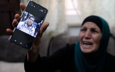 La mère d'un Palestinien atteint de troubles autistiques que la police aurait tué, croyant qu'il était armé, pleure en montrant la photo de son fils sur son téléphone au domicile familial de Jérusalem-Est, le 30 mai 2020 (Crédit : Ahmad GHARABLI / AFP)