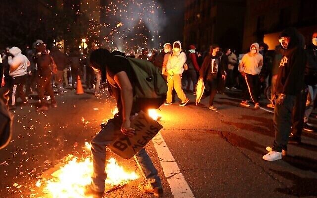 Un manifestant tente d'éteindre un incendie de poubelle lors d'une manifestation déclenchée par la mort de George Floyd le 29 mai 2020 à Oakland, en Californie. (Crédit : Justin Sullivan / Getty Images / AFP) Un manifestant tente d'éteindre un incendie de poubelle lors d'une manifestation déclenchée par la mort de George Floyd le 29 mai 2020 à Oakland, en Californie. (Crédit : Justin Sullivan / Getty Images / AFP)